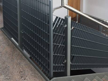 Dovetail pressure locked steel grating infill panels are installed on stair railings in the passageway.