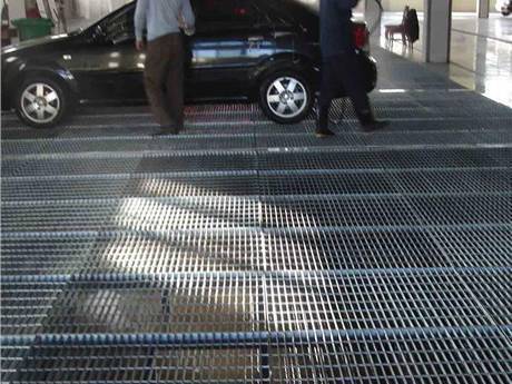This is a indoor parking lot with two people and a car on welded bar grating floor.