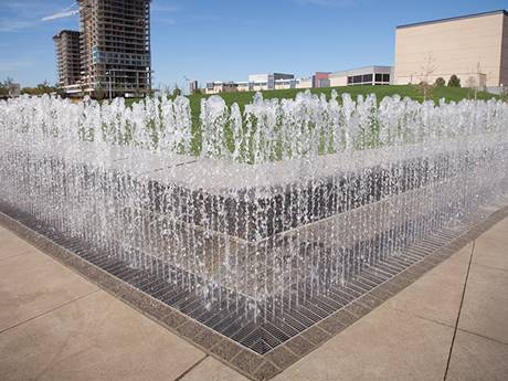 The fountain is sprinkling water at a corner drain of a rectangular steel grating.