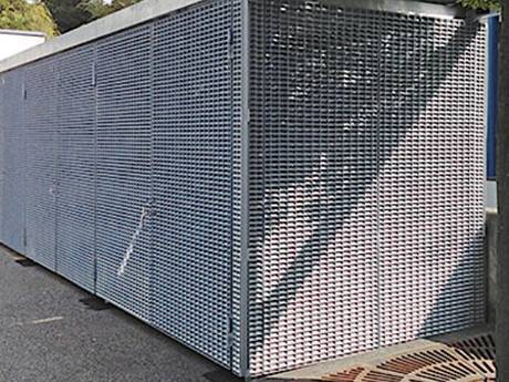 A container made of galvanized steel grating is in the street.