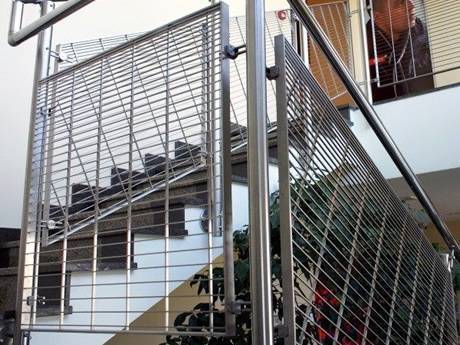 Dovetail pressure locked steel grating infill panels are installed on stair railings indoors.