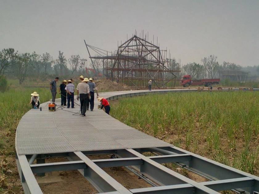 Varios trabajadores están instalando la pasarela de rejilla de acero en los campos.