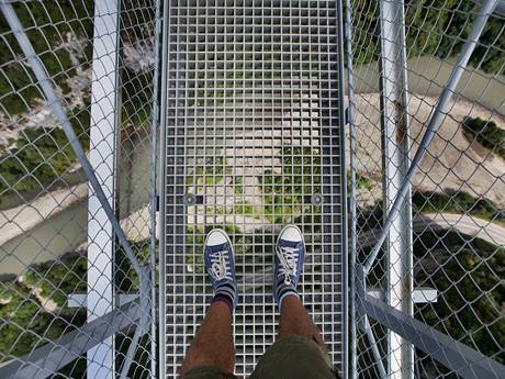 A person standing on suspension bridge and overlook the view under his feet.