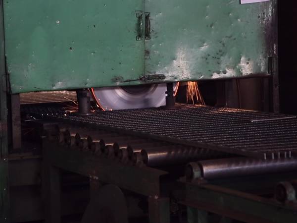 Una máquina de corte está cortando rejillas de acero soldado.