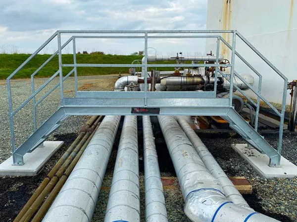 Steel grating pedestrian bridge installed over pipelines.
